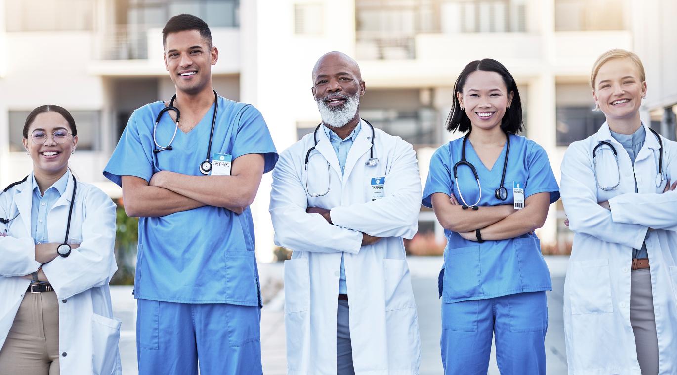 five physicians standing shoulder to shoulder with arms crossed over their chests looking happy